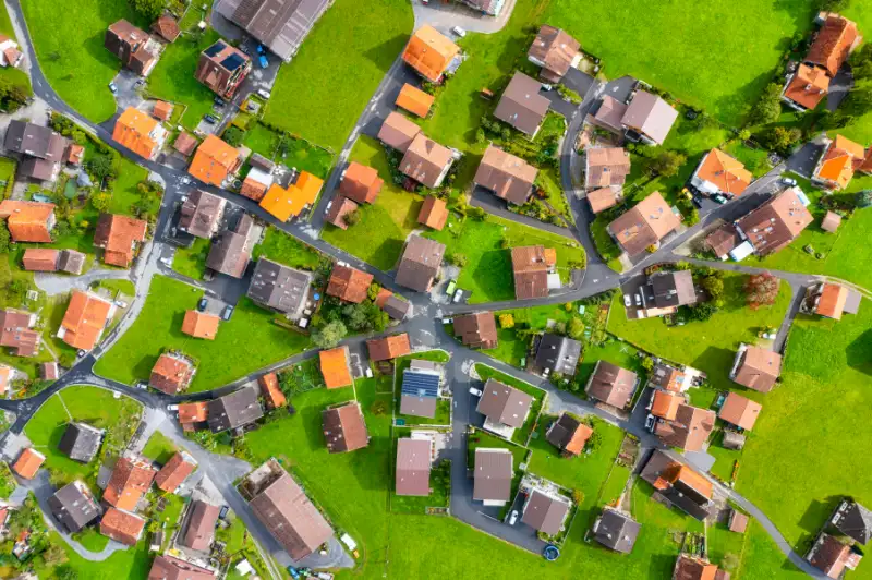 Welche Vorteile bietet Google Street View? 18 Fotograf Hannover - Eine Luftaufnahme eines Vorortviertels mit zahlreichen Häusern mit roten und braunen Dächern. Das Gebiet ist durch gewundene Straßen unterteilt und jedes Haus ist von grünen Rasenflächen umgeben, die ein Patchwork-Muster bilden. Fotograf in der Nähe.