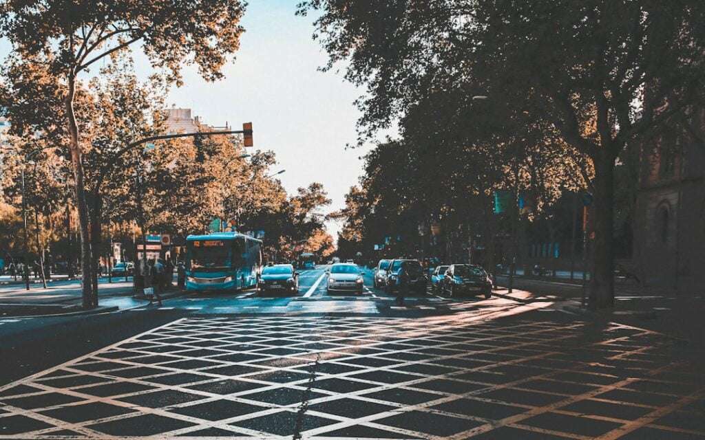 Was kostet Google Street View für dich? 12 Fotograf Hannover Straßenkreuzung in der Stadt mit einem Bus und mehreren Autos, die an einer Ampel anhalten. Bäume säumen beide Seiten der Straße, und im Hintergrund sind teilweise Gebäude zu sehen. Die Zebrastreifenmarkierungen auf der Straße sind im Vordergrund deutlich zu erkennen.