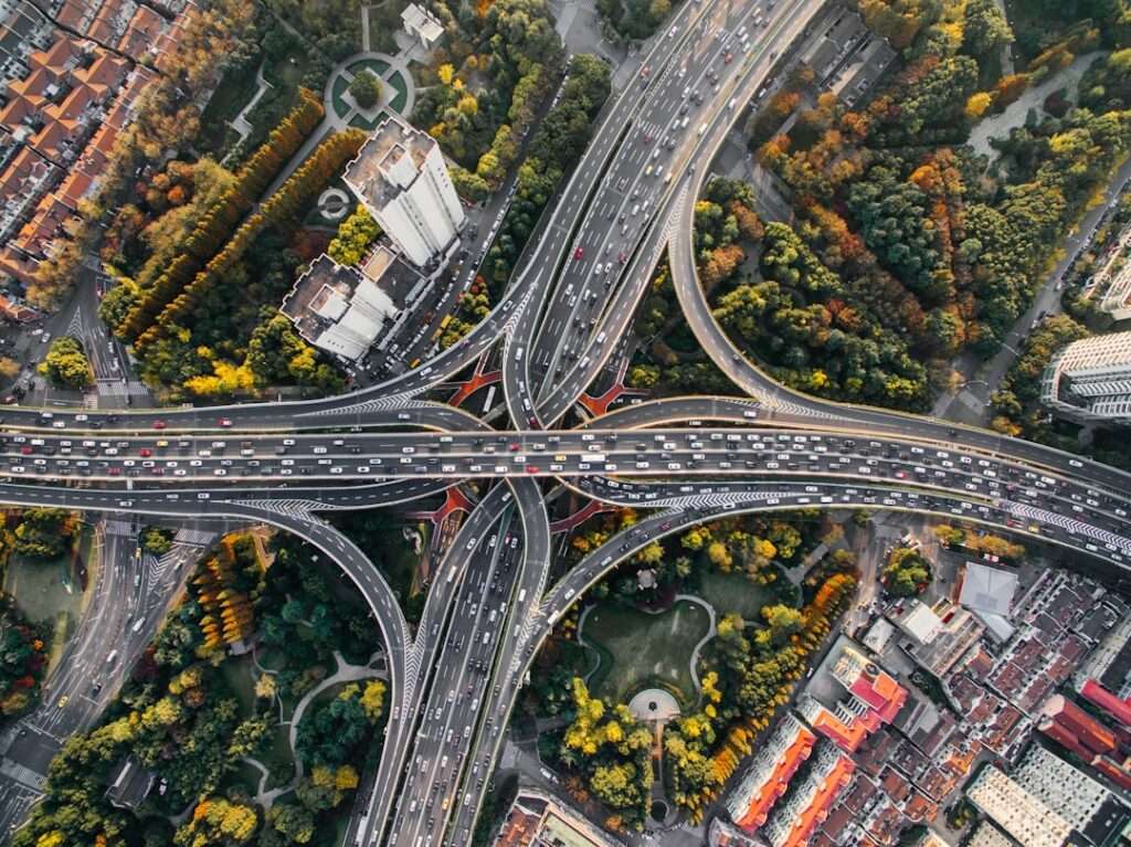 Drohnen Aufnahme: Effektive Luftbildaufnahmen 7 Fotograf Hannover - Luftaufnahme eines komplexen Autobahnkreuzes mit mehreren Fahrspuren, die in verschiedene Richtungen fließen. Das Kreuz ist von dichten grünen Bäumen und städtischen Gebäuden umgeben. Das Foto zeigt eine Mischung aus Natur und städtischer Infrastruktur. Fotograf in der Nähe.