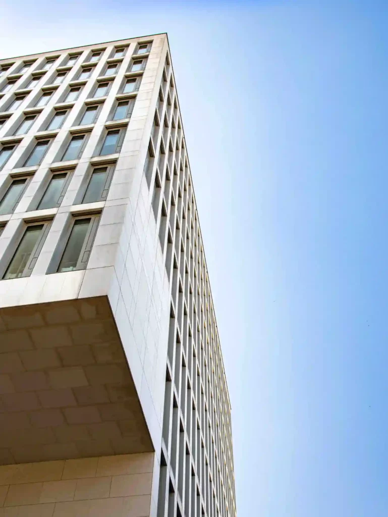Home 5 Fotograf Hannover Untersicht eines modernen, hohen Gebäudes mit einem gitterartigen Fenstermuster an der Fassade vor einem klaren blauen Himmel. Das Gebäude scheint ein Büro- oder Geschäftsgebäude mit einem schlanken, minimalistischen Design zu sein. Fotograf in der Nähe.