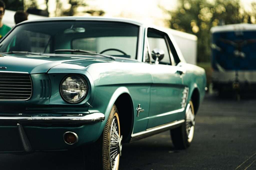 Fotoshooting mit Auto: Meine Leidenschaft für schöne Bilder 11 Fotograf Hannover Ein türkisfarbener Ford Mustang steht auf einer gepflasterten Fläche. Das Auto hat ein klassisches Design mit einem Chromgrill und runden Scheinwerfern. Im Hintergrund sind Bäume und ein Gebäude zu sehen. Das Foto wurde schräg von vorne links vom Fahrzeug aufgenommen. Fotograf in der Nähe.